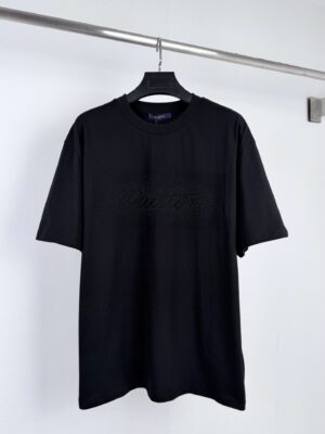 P120 LOUIS VUITTON 路易 LV 钢柱压印留白标识装饰短袖T恤 洗涤建议：反转入袋、15分钟快洗或手洗、避免烘干 SIZE:XS S M L 本款T恤以错视设计流露雅致意趣。饰钉化身为一团深浅渐变的椭圆形云朵，令横贯胸前的手写体标识于留白空间跃然显现，仿佛用指尖在凝结水汽的表面作画，营造朦朦胧胧的视觉幻象。 12支粗纱赋予布面清晰的斜纹肌理与天然的粗粝质感，手感干爽挺括、抗皱性强，有效避免低克重面料的软塌与透视问题。精梳工艺剔除短绒与杂质，确保纱线光洁匀整，接触皮肤时虽有颗粒感却无刺痒。领口高支高密编织使罗纹细腻紧实、弹性优异，能稳固锁定领型并抵抗反复穿脱的拉扯。厚重面料能有效分散饰钉压印时的局部应力，防止布面因高温高压而产生皱缩或变形，为精密压印工艺提供稳定基底。 胸前渐变标识通过半圆珠铝片高温压印技术精妙构建： 每一颗半圆珠铝片均为微小的半球形金属件，表面经镀膜处理，具备细腻的微光反射质感；压印时通过定制模具在高温条件下将铝片逐颗嵌入棉布纤维间隙，温度使棉纤维局部软化，压力将铝片底座压入织物，冷却后纤维回弹包裹铝片边缘，形成牢固的物理嵌合，无需胶水即可抵御日常穿脱与水洗。 深浅渐变的视觉效果依赖于铝片规格的精密排布：高密度的铝片聚集形成标识的深色核心区域，低密度的铝片散布于边缘形成云雾般的朦胧过渡，最终以点阵化的方式拼出手写体标识的完整轮廓，营造出仿佛指尖在凝结水汽表面作画的错视幻象。