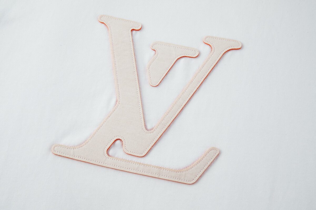 P110 LOUIS VUITTON 皮革刺绣标识短袖 面料：采用32支双纱精梳棉。 面料：螺纹采用1*1配套索罗娜。 辅料：浅粉面布切割复合羊皮，侧边带有人工油边工艺。高度还原原版LV标识辅料。 工艺：刺绣缝线，底部缝线定位后面上多缝一层使辅料与衣服牢牢凝固。 工艺：后服3D立体刺绣工艺,以品字母做为点点缀，整针数约为4800针。 本款T恤玩味2026秋冬秀场的视觉先锋，为轻盈棉质针织融入激光切割LV标识，其撞色毛毡底垫恰似品牌标志性VVN皮革的染色边缘，以考究笔触营造悬浮效果。背后的标识刺绣再添雅致一笔。 辅料：定制1：1洗水商标 辅料：定制1：1皮革标识 工艺：定制1：1刺绣标识 尺码：S-M-L-X 颜色：白 款号：86137-818