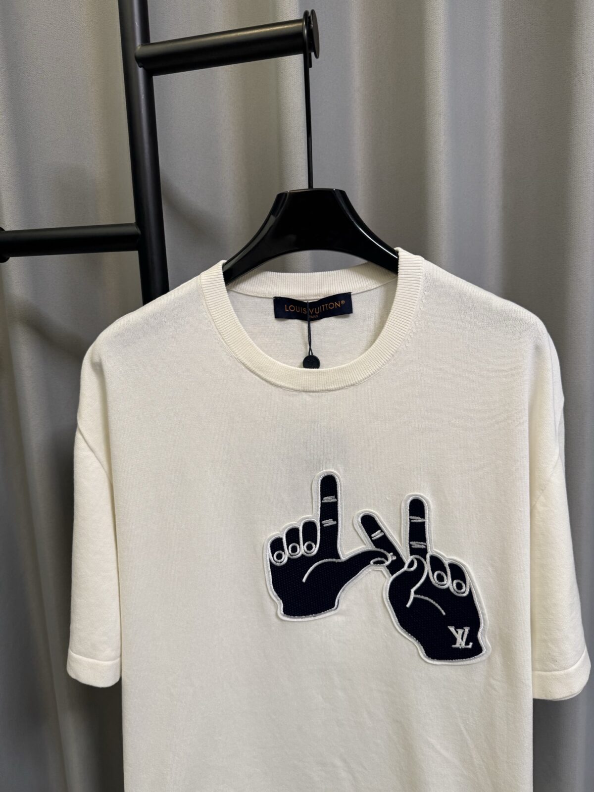 P155 【高端复刻】 𝐋𝐨𝐮𝐢𝐬 𝐕𝐮𝐢𝐭𝐭𝐨𝐧/路易 26SS lv手势刺绣针织短袖T恤（米白） LV 以趣味手势元素打造的创意系列短袖，用针织面料与立体刺绣工艺，打造兼具质感与个性的小众款。 🔹 面料与质感 核心面料：甄选LV 定制针织面料，布面细腻软糯，自带柔和哑光质感，上身轻薄透气，垂坠感优异，久穿不易起球变形。 穿着体验：面料亲肤透气，吸湿排汗性优异，夏季穿着清爽不闷汗；触感顺滑亲肤，不扎肤、不闷热，日常穿着舒适自在。 版型表现：合身直筒版型，修饰肩线与身形比例；圆领设计利落干练，自带简约高级氛围，适配多种穿搭场景。 🔹 工艺与细节 核心手势刺绣工艺： 胸口位置采用趣味手势刺绣，以藏蓝色为主体，搭配白色轮廓线，其中一只手上带有 LV 字母标识，刺绣针脚细密饱满，边缘无毛边，质感立体精致。在极简的米白色针织衣身上，这个创意手势刺绣是整件 T 恤的灵魂亮点。 细节做工： 领口采用罗纹收边，走线工整细密，反复穿着不易松垮变形； 袖口、下摆采用罗纹锁边，做工精细，不易脱线； 领标、洗水标等辅料齐全，完整还原正品配置，细节拉满。 Size：s/m/l/xl/