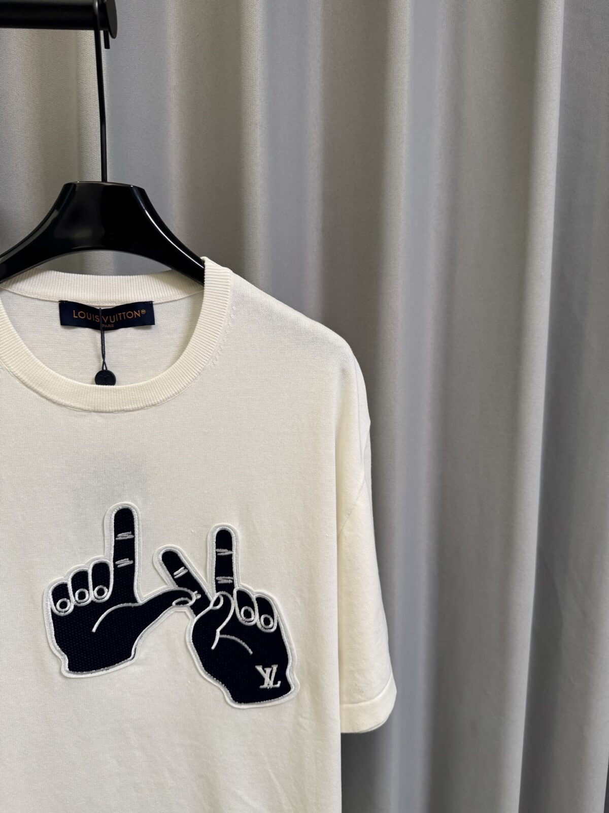P155 【高端复刻】 𝐋𝐨𝐮𝐢𝐬 𝐕𝐮𝐢𝐭𝐭𝐨𝐧/路易 26SS lv手势刺绣针织短袖T恤（米白） LV 以趣味手势元素打造的创意系列短袖，用针织面料与立体刺绣工艺，打造兼具质感与个性的小众款。 🔹 面料与质感 核心面料：甄选LV 定制针织面料，布面细腻软糯，自带柔和哑光质感，上身轻薄透气，垂坠感优异，久穿不易起球变形。 穿着体验：面料亲肤透气，吸湿排汗性优异，夏季穿着清爽不闷汗；触感顺滑亲肤，不扎肤、不闷热，日常穿着舒适自在。 版型表现：合身直筒版型，修饰肩线与身形比例；圆领设计利落干练，自带简约高级氛围，适配多种穿搭场景。 🔹 工艺与细节 核心手势刺绣工艺： 胸口位置采用趣味手势刺绣，以藏蓝色为主体，搭配白色轮廓线，其中一只手上带有 LV 字母标识，刺绣针脚细密饱满，边缘无毛边，质感立体精致。在极简的米白色针织衣身上，这个创意手势刺绣是整件 T 恤的灵魂亮点。 细节做工： 领口采用罗纹收边，走线工整细密，反复穿着不易松垮变形； 袖口、下摆采用罗纹锁边，做工精细，不易脱线； 领标、洗水标等辅料齐全，完整还原正品配置，细节拉满。 Size：s/m/l/xl/