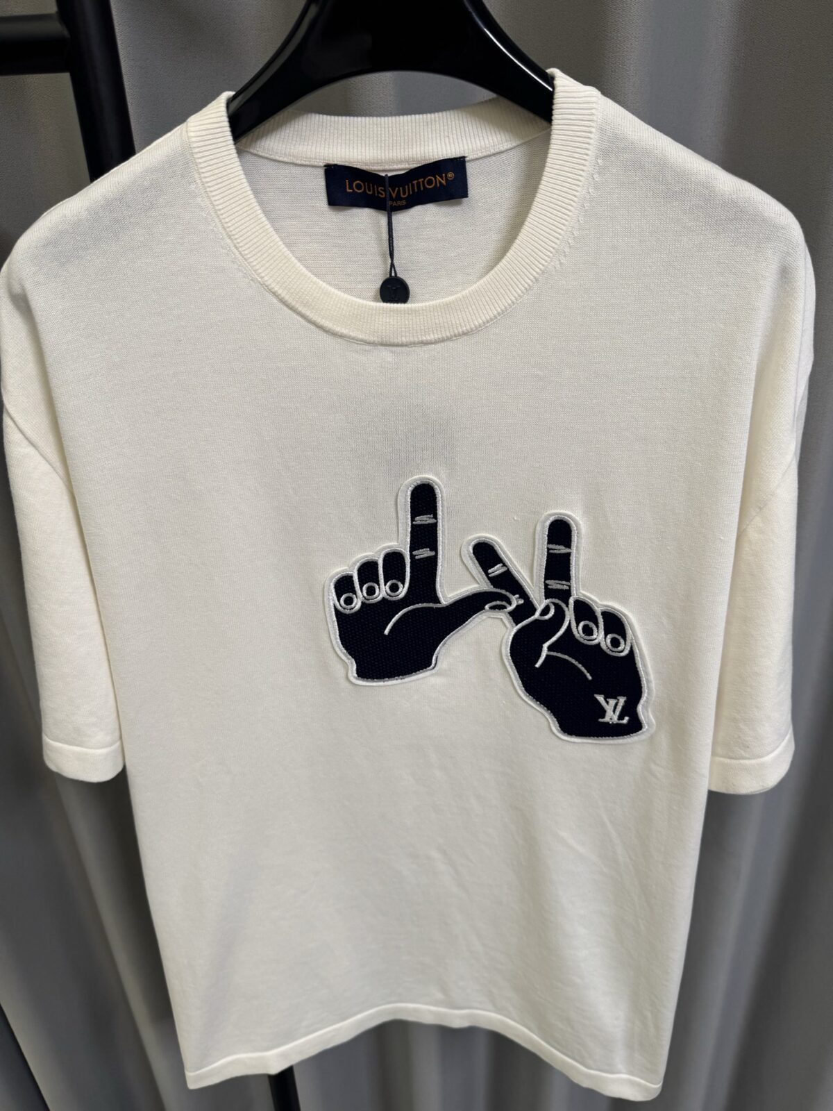 P155 【高端复刻】 𝐋𝐨𝐮𝐢𝐬 𝐕𝐮𝐢𝐭𝐭𝐨𝐧/路易 26SS lv手势刺绣针织短袖T恤（米白） LV 以趣味手势元素打造的创意系列短袖，用针织面料与立体刺绣工艺，打造兼具质感与个性的小众款。 🔹 面料与质感 核心面料：甄选LV 定制针织面料，布面细腻软糯，自带柔和哑光质感，上身轻薄透气，垂坠感优异，久穿不易起球变形。 穿着体验：面料亲肤透气，吸湿排汗性优异，夏季穿着清爽不闷汗；触感顺滑亲肤，不扎肤、不闷热，日常穿着舒适自在。 版型表现：合身直筒版型，修饰肩线与身形比例；圆领设计利落干练，自带简约高级氛围，适配多种穿搭场景。 🔹 工艺与细节 核心手势刺绣工艺： 胸口位置采用趣味手势刺绣，以藏蓝色为主体，搭配白色轮廓线，其中一只手上带有 LV 字母标识，刺绣针脚细密饱满，边缘无毛边，质感立体精致。在极简的米白色针织衣身上，这个创意手势刺绣是整件 T 恤的灵魂亮点。 细节做工： 领口采用罗纹收边，走线工整细密，反复穿着不易松垮变形； 袖口、下摆采用罗纹锁边，做工精细，不易脱线； 领标、洗水标等辅料齐全，完整还原正品配置，细节拉满。 Size：s/m/l/xl/