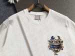 P80 迪奥 Dior密蜂皇冠徽章刺绣短袖T恤 采用100%精梳双股棉平纹针织面料织造，经预缩水洗工艺处理，布面平整光洁且抗缩率稳定，垂坠挺括兼具亲肤透气属性 廓形为Oversize落肩版型，圆领采用双针包边工艺，领口内置弹力罗纹，久洗不易变形。前中核心徽章图案采用多色立体盘绣工艺，以蓝、金、棕三色分层刺绣，通过长短针、打籽绣等针法塑造浮雕质感，将皇家纹章、骏马、鹰羽与品牌标志性蜜蜂元素精准呈现，绣线光泽度饱满且线迹密度均匀，边缘无跳线毛边 2026ss官方同步 高版本 高品质 时尚个性 百搭潮流 纯原品质 原版面料 吊牌 领标 水洗麦 三标齐全 颜色：白色 码数：S M L XL