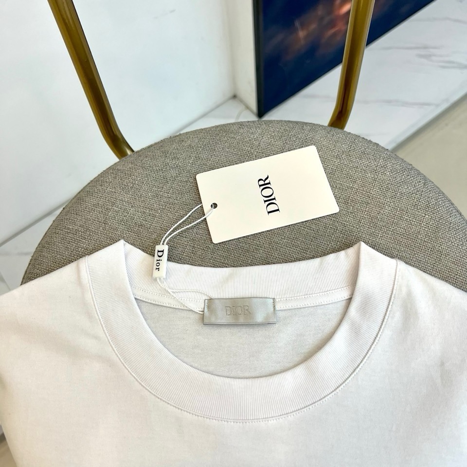 P75 Dio迪奥2026春夏新品短袖T恤，以极简主义为设计内核，经典圆领剪裁贴合颈部线条，宽松廓形包容各种身形，营造随性自在的穿着氛围。衣身采用优质棉质面料，触感柔软亲肤，透气吸汗，完美适配春夏季节的穿着需求。左胸位置的金属质感字母标识是点睛之笔，立体浮雕工艺赋予单品低调奢华的辨识度，在纯色基底上折射出细腻光泽，打破单调又不失高级感。整体风格简约而不简单，既有基础款的百搭属性，又通过精致细节提升时尚完成度，这件T恤诠释了当代都市男装的精致态度，将舒适实穿与设计美学完美融合，是春夏衣橱不可或缺的品质之选，让你在每一个场合都能展现从容自信的个人魅力。码数：S-2XL