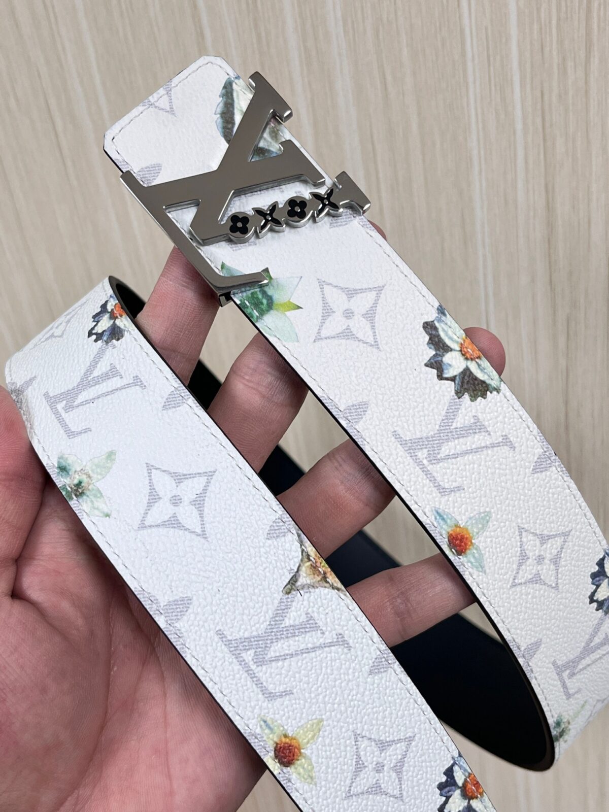 P150 当季新款，LV Initiales Monogram Flower系列40毫米可翻转腰带重新诠释了经典的LV标志，以唤起运动和情感的花纹。在画布一侧，Monogram通过添加白色和金色调的花朵，生动地描绘了每一片花瓣，赋予了它新的生命。白色的皮革背面同样优雅。 白花印百合花