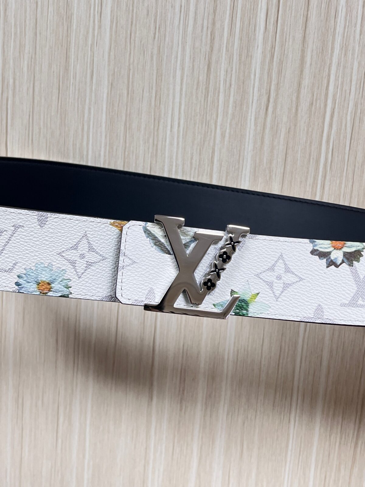 P150 当季新款，LV Initiales Monogram Flower系列40毫米可翻转腰带重新诠释了经典的LV标志，以唤起运动和情感的花纹。在画布一侧，Monogram通过添加白色和金色调的花朵，生动地描绘了每一片花瓣，赋予了它新的生命。白色的皮革背面同样优雅。 白花印百合花