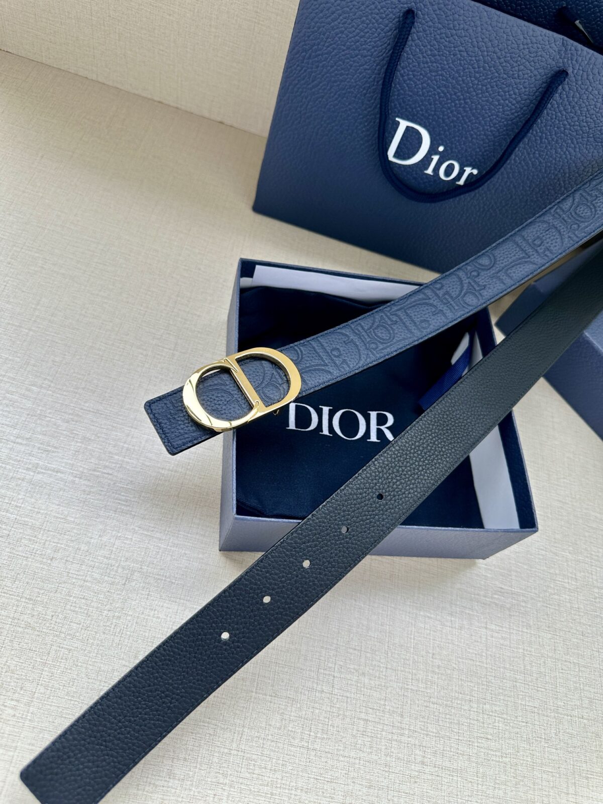Dior Gravity 印花效果皮革，以牛皮革融合压花工艺，演绎经典的 Oblique 印花，展现 Dior 的精湛工艺。另一面则采用同色调光滑牛皮革。长度可调节，可搭配各式 35 毫米腰带扣。 /